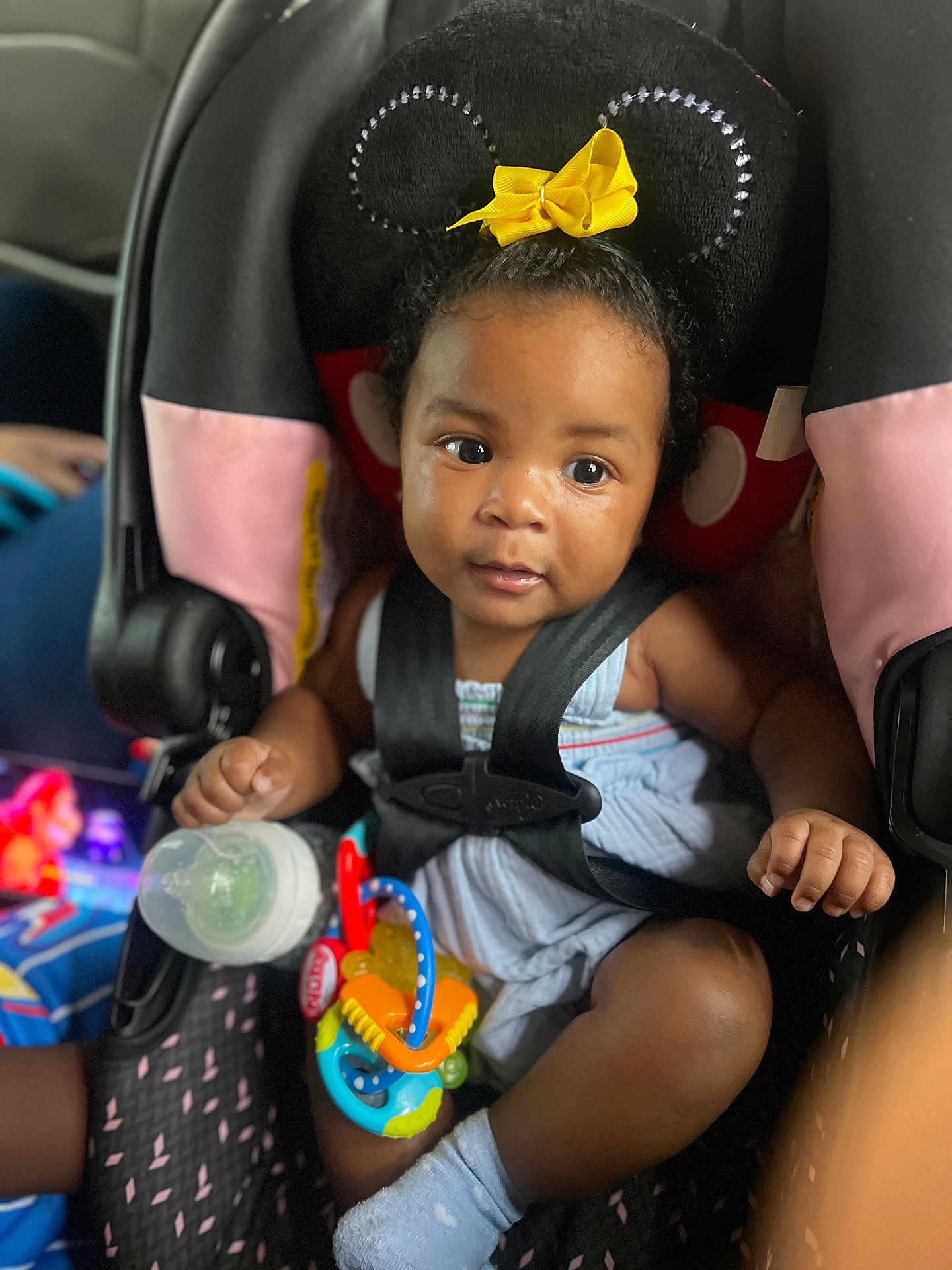 Charm Ross joined the competition — help win amazing prizes! baby, child, car_seat, toy, bottle, headband, minnie_mouse_ears, yellow_bow, sitting, curious, black_hair, blue_outfit, sock, infant, seat_belt, indoors, cute, face, portrait, closeup