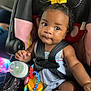 Charm Ross is registered to the contest to win money with this photo: baby, child, car_seat, toy, bottle, yellow_bow, curly_hair, black_hair, clothing, infant, sitting, safety_harness, close_up, indoor, person, cute, bright_eyes, colorful, playful, adorable