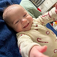 Makaio is registered to the contest to win money with this photo: baby, blanket, candy_cane, child, cozy, cute, expression, face, furniture, happy, head, indoor, infant, onesie, person, portrait, reaching_out, room, smiling, soft_texture