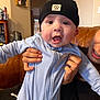 Makaio is registered to the contest to win money with this photo: baby, beanie, big_eyes, blue_onesie, braces, close_up, couch, hands, hat, indoor, infant, living_room, mouth_open, partial_face, person, portrait, smile, sofa, surprised_expression, zipper