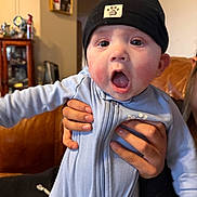 Makaio is registered to the contest to win money with this photo: baby, beanie, cabinet, cheeks, close_up, expression, eyes, family, furniture, hands, hat, indoor, infant, living_room, onesie, open_mouth, portrait, skin, sofa, surprised
