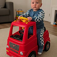 Joseph is registered to the contest to win money with this photo: baby, blue_outfit, carpet, checkered_pattern, child, cute, door, floor, furniture, home, indoor, living_room, playtime, red_toy, serious_expression, steering_wheel, toddler, toy_truck, toy_vehicle, young_child