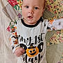 baby, infant, child, face, expression, onesie, clothing, text, pumpkin, halloween, quilt, pattern, colorful, fabric, bed, cute, portrait, indoor, celebration, holiday