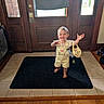 toddler, child, smiling, barefoot, yellow_overalls, bunny_purse, black_rug, wooden_door, tile_floor, hardwood_floor, indoor, happy, person, young_child, small_bag, home, natural_light, front_door, cute, playful