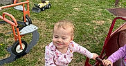 Ellie is registered to the contest to win money with this photo: casual_clothing, child, daylight, fun, grass, happy, metal, outdoor, pajamas, park, person, play, play_equipment, playground, smiling, steering_wheel, swing, toddler, toy_truck, young_child
