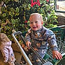 toddler, child, shopping_cart, christmas_tree, holiday_decorations, smiling, indoor, window, pine_cones, red_star_ornament, lights, pajamas, cart, person, floor, clothing, boots, pink_hoodie, patterned_pants, festive