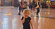 Angel joined the competition — help win amazing prizes! child, indoor, american_flag, people, walking, floor, windows, architecture, public_space, casual_clothing, blonde_hair, black_outfit, shoes, large_hall, light, background, tourists, reflection, crowd, daylight