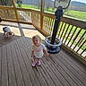 Angel joined the competition — help win amazing prizes! child, toddler, deck, wooden_floor, binocular_viewer, outdoor, railing, greenery, grass, hill, sunlight, shadow, curious, crawling, standing, clothing, shoes, nature, fence, playful