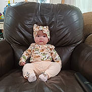 Camila is registered to the contest to win money with this photo: baby, child, infant, floral_outfit, headband, armchair, leather, indoor, furniture, cute, sitting, portrait, small_person, sock, expression, looking_at_camera, home, room, comfort, adorable