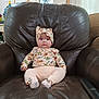 baby, child, infant, floral_outfit, headband, armchair, leather, indoor, furniture, cute, sitting, portrait, small_person, sock, expression, looking_at_camera, home, room, comfort, adorable