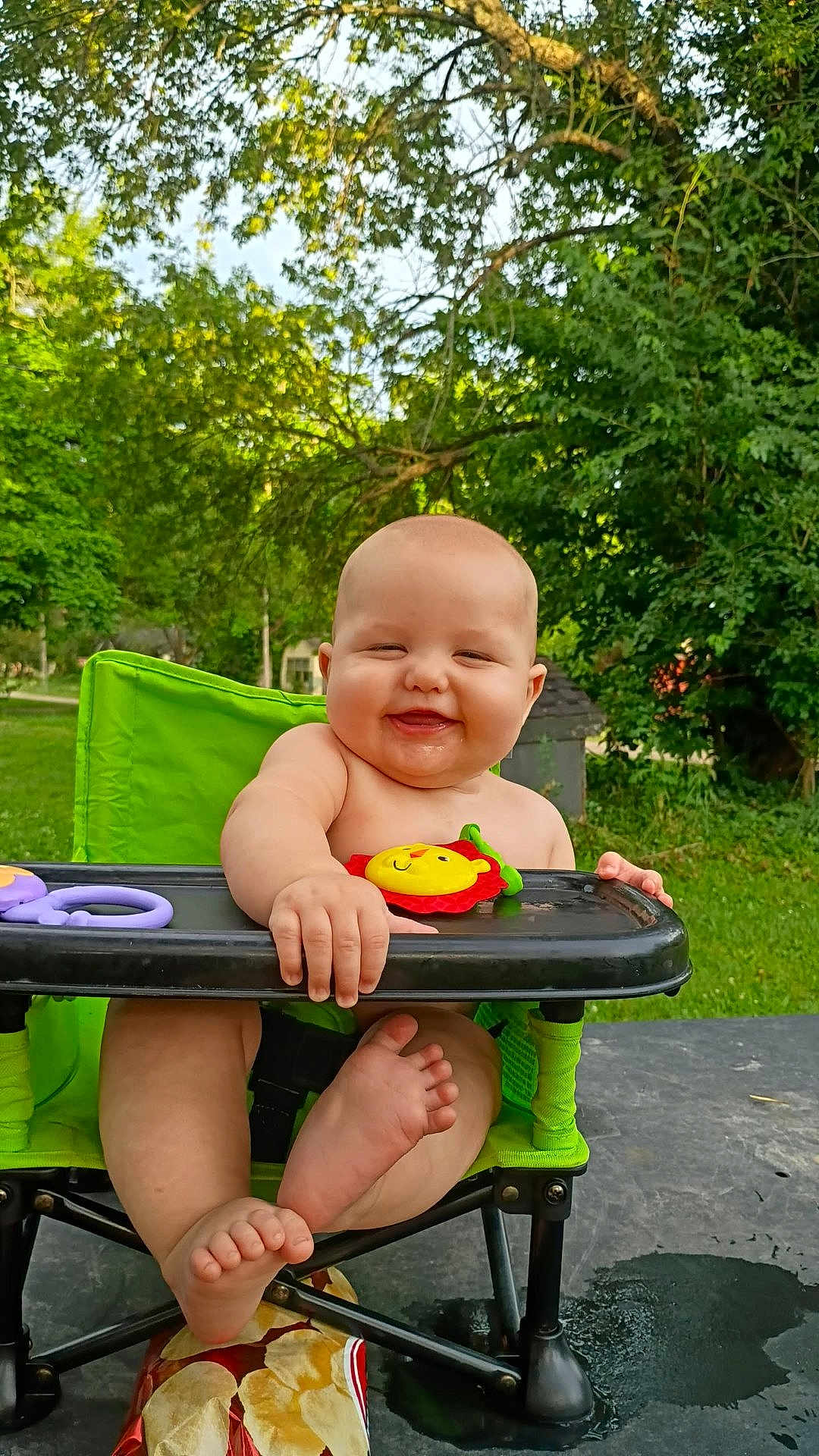 Casey is registered to the contest to win money with this photo: baby, child, smile, high_chair, outdoor, greenery, happy, toes, nature, sunlight, playful, cute, infant, seat, plastic_toy, summer, grass, tree, grass_lawn, baby_toy
