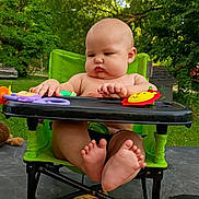 Casey is registered to the contest to win money with this photo: baby, child, high_chair, toy, outdoor, greenery, trees, feet, hands, plastic_toy, summer, nature, sunlight, table, snack_bag, infant, cute, chubby, seat, playtime