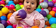 Adriana a rejoint le concours — aidez-le/la à gagner de superbes lots ! toddler, child, ball_pit, colorful_balls, play, fun, happy, indoor, casual_clothing, pigtails, pink_sweater, white_socks, expressive_face, young_child, netting, background, bright_colors, active, cute, playtime