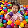 toddler, child, ball_pit, colorful_balls, play, fun, happy, indoor, casual_clothing, pigtails, pink_sweater, white_socks, expressive_face, young_child, netting, background, bright_colors, active, cute, playtime