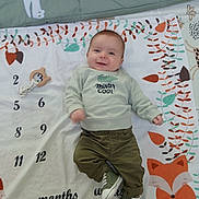 émile participe au concours pour gagner de l'argent avec cette photo : baby, smiling, infant, clothing, sweatshirt, pants, shoes, milestone_blanket, fox, toy, indoor, cute, child, person, face, happy, lying_down, green, white, orange