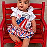 baby, child, red_bench, american_flag, headband, dress, shoes, 4th_of_july, holiday, cute, portrait, sitting, celebration, face, outdoor, person, fashion, smile, festive, colorful