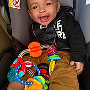 Gabriel is registered to the contest to win money with this photo: baby, car_seat, toy, smiling, child, infant, seatbelt, colorful_toy, clothing, happy, indoors, person, cute, play, holding, sitting, closeup, face, young_child, casual
