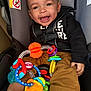 baby, car_seat, toy, smiling, child, infant, seatbelt, colorful_toy, clothing, happy, indoors, person, cute, play, holding, sitting, closeup, face, young_child, casual