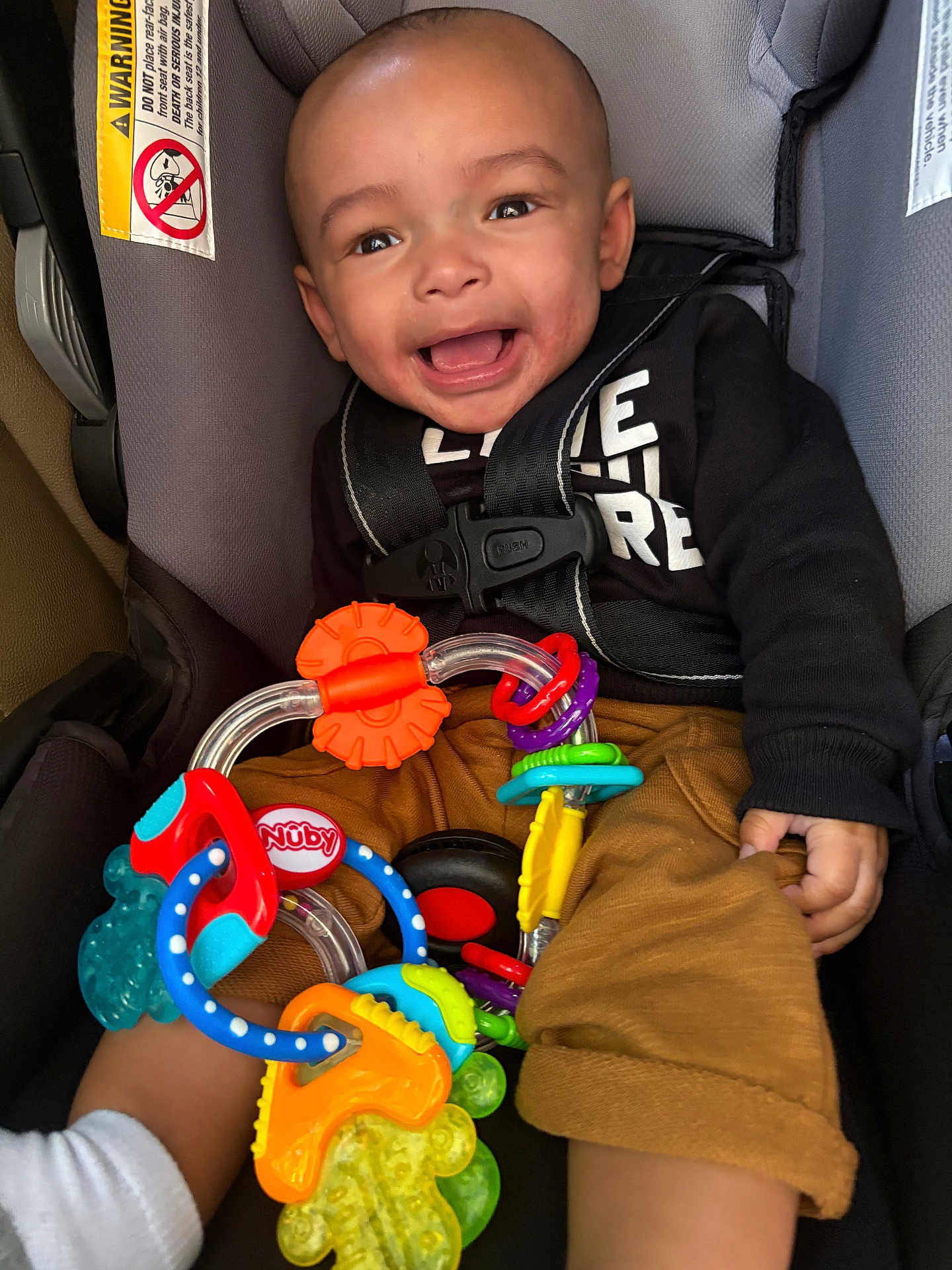Gabriel is registered to the contest to win money with this photo: baby, car_seat, toy, smiling, child, infant, seatbelt, colorful_toy, clothing, happy, indoors, person, cute, play, holding, sitting, closeup, face, young_child, casual