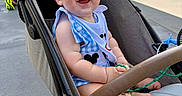 Colson is registered to the contest to win money with this photo: baby, stroller, smile, child, outdoor, sunlight, happy, blue_clothing, seat, footwear, toy, urban, building, person, infant, casual, daytime, cute, joyful, baby_bib