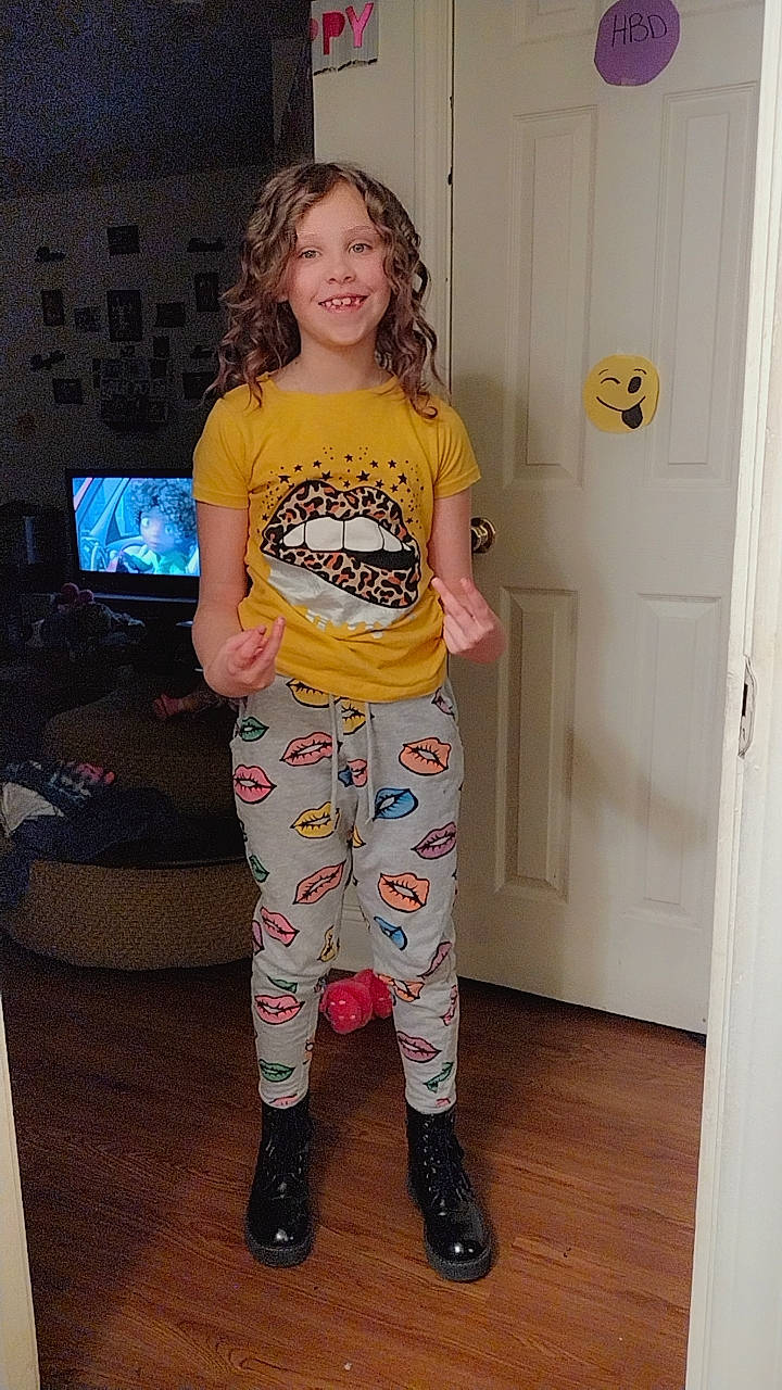 Adelynn is registered to the contest to win money with this photo: active_pants, boot, door, face, fashion_design, fun, head, human_leg, joy, knee, pajamas, pattern, peach, person, room, sleeve, smile, t_shirt, television, thigh
