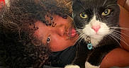Flips is registered to the contest to win money with this photo: person, cat, tuxedo_cat, pet, cuddling, close_up, portrait, green_eyes, whiskers, pink_nose, black_and_white, curly_hair, indoor, chair, cozy, companion, collar, tag, selfie, affection