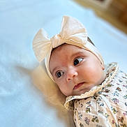 Camila a rejoint le concours — aidez-le/la à gagner de superbes lots ! baby, infant, headband, bow, floral_outfit, lying_down, soft_surface, closeup, portrait, cute, adorable, child, young, face, expression, indoors, soft_light, skin, eyes, headwear