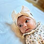 baby, infant, headband, bow, floral_outfit, lying_down, soft_surface, closeup, portrait, cute, adorable, child, young, face, expression, indoors, soft_light, skin, eyes, headwear