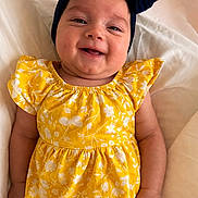 Alaina is registered to the contest to win money with this photo: baby, child, smiling, yellow_dress, headband, bow, infant, portrait, happy, cute, lying_down, white_background, clothing, person, skin, face, hand, baby_fashion, indoors, young_child