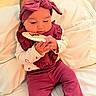 baby, infant, child, headband, maroon_outfit, plaid, wooden_plaque, milestone, cushion, white_background, cute, curious, hands, sitting, indoors, portrait, soft_lighting, clothing, cozy, young_child
