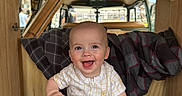 Braxton joined the competition — help win amazing prizes! baby, smiling, infant, sitting, onesie, white_socks, plaid_blanket, wooden_panels, van, camper, interior, happy, cute, child, indoors, face, person, clothing, toy, pacifier_clip