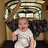 baby, smiling, infant, sitting, onesie, white_socks, plaid_blanket, wooden_panels, van, camper, interior, happy, cute, child, indoors, face, person, clothing, toy, pacifier_clip