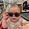 Braxton joined the competition — help win amazing prizes! baby, child, sunglasses, shopping_cart, hand_holding, store, aisle, indoor, person, cute, fashion, infant, toddler, clothing, retail, bright, blurred_background, raising_hand, casual, accessory