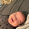 baby, smiling, onesie, star_pattern, bed, blanket, pillow, face, head, infant, happy, closeup, sleepwear, person, child, cute, cozy, indoor, portrait, resting