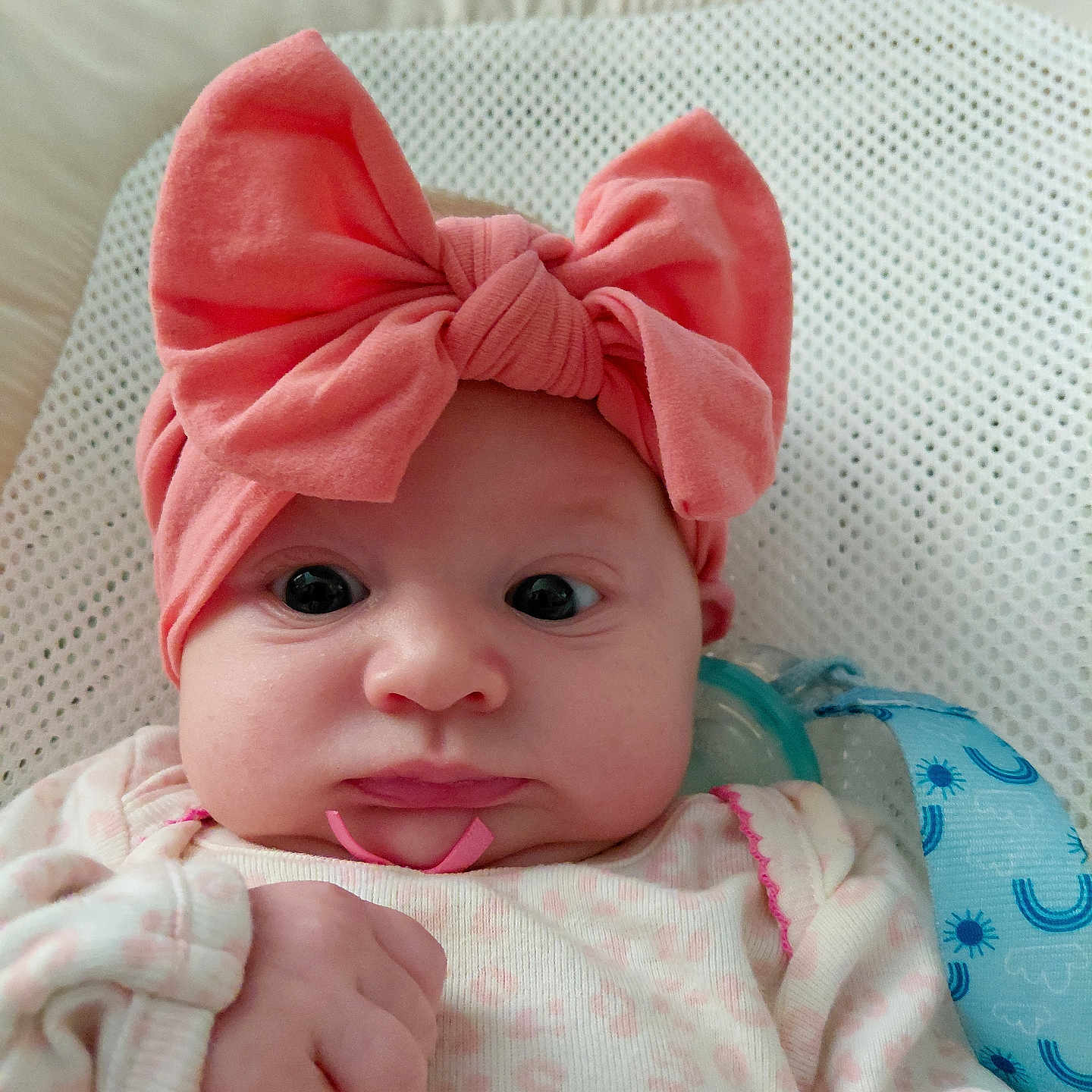Willow is registered to the contest to win money with this photo: baby, infant, headband, pink_bow, clothing, face, hand, fist, cushion, pattern, indoor, portrait, cute, wide_eyes, soft_fabric, newborn, child, wearing, expression, comfortable