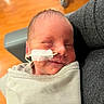 Jaxon is registered to the contest to win money with this photo: newborn, baby, infant, sleeping, face, portrait, swaddled, blanket, medical_tube, nasal_cannula, hospital, parent, adult, arms, close_up, indoor, wood_floor, gray_clothing, peaceful, family