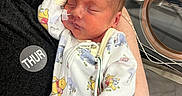 Jaxon is registered to the contest to win money with this photo: newborn, baby, infant, sleeping, hospital, medical_equipment, onesie, blanket, parent, arms, face, closed_eyes, cuddling, portrait, indoors, nursery, wires, monitor, cartoon_print, peaceful