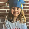 blue_cap, brick_wall, casual_clothing, celebration, child, cute, face, fun, girl, graduation_cap, happy, headwear, long_hair, outdoor, person, portrait, smiling, white_shirt, yellow_tassel, young