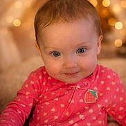 Peyton joined the competition — help win amazing prizes! baby, child, pink_clothing, heart_pattern, strawberry_patch, smile, face, blue_eyes, soft_lighting, bokeh, warm_colors, indoors, portrait, cute, infant, cozy, background_blur, happy, sitting, onesie