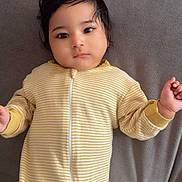 Asees is registered to the contest to win money with this photo: baby, child, infant, portrait, lying_down, couch, indoors, yellow, striped_clothing, romper, zipper, dark_hair, brown_eyes, face, hands, calm, cute, soft_lighting, furniture, cozy