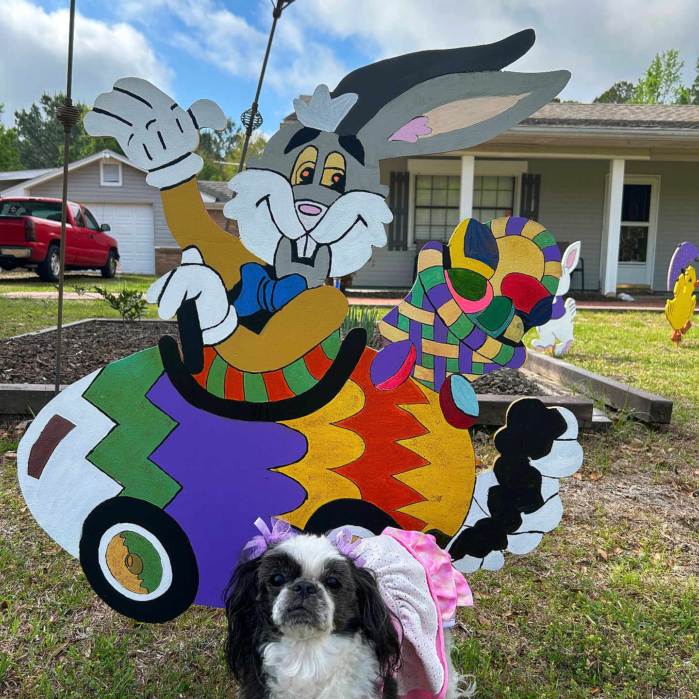 Nina joined the competition — help win amazing prizes! dog, pet, costume, pink_dress, black_and_white, grass, yard, house, wooden_cutout, cartoon_rabbit, colorful, outdoor, sunny, vehicle_cutout, flowerbed, residential, tree, blue_sky, clouds, truck