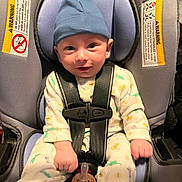 Jesse is registered to the contest to win money with this photo: baby, infant, child, car_seat, buckled, blue_cap, pajamas, pacifier, smiling, portrait, sitting, indoors, vehicle, safety_harness, carseat, face, eyes, clothing, happy, photography
