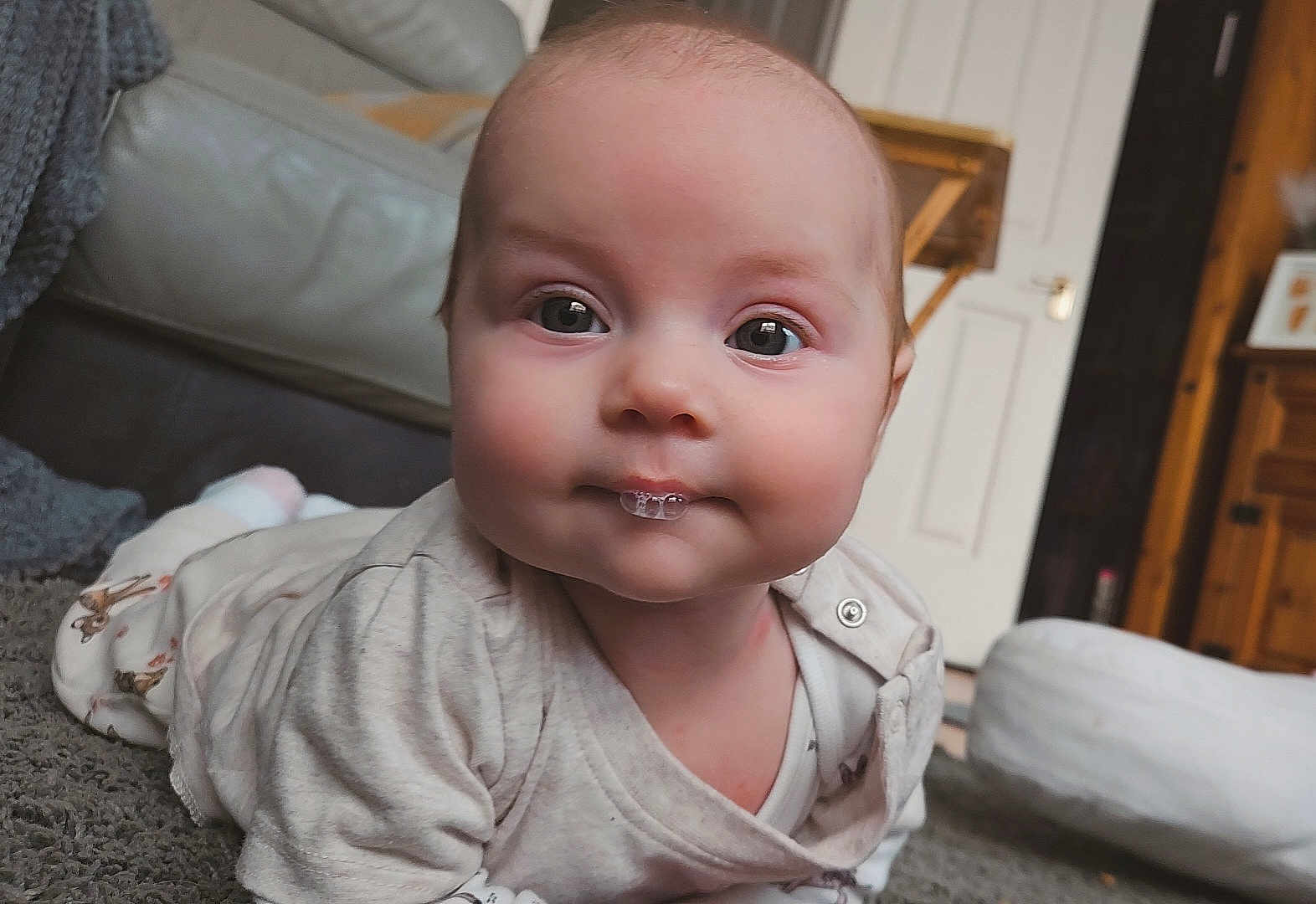 Lilith is registered to the contest to win money with this photo: baby, infant, face, eyes, bubble, carpet, home_interior, furniture, door, wood, clothing, tummy_time, cute, child, indoor, portrait, skin, expression, person, cozy