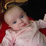 Emma joined the competition — help win amazing prizes! baby, infant, face, blue_eyes, pink_onesie, heart_pattern, person, indoor, closeup, child, curious, holding, red_shirt, crib, window_air_conditioner, furniture, cozy, portrait, skin, cute