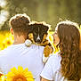 puppy, dog, couple, sunflower, field, outdoor, pet, young_adult, white_shirt, nature, summer, sunlight, greenery, affection, back_view, holding, tattoo, casual_clothing, curly_hair, animal
