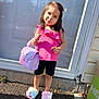 child, girl, pink_top, black_shorts, handbag, fluffy_slippers, standing, outdoor, door, pavement, sunlight, playful, posing, hair_clip, smiling, cute, fashion, accessory, footwear, sidewalk