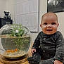 Alice participe au concours pour gagner de l'argent avec cette photo : baby, infant, smiling, fishbowl, goldfish, plant, table, onesie, indoor, window_blind, cabinet, teddy_bear, portrait, gorilla_poster, wooden_surface, cute, child, sitting, decor, home