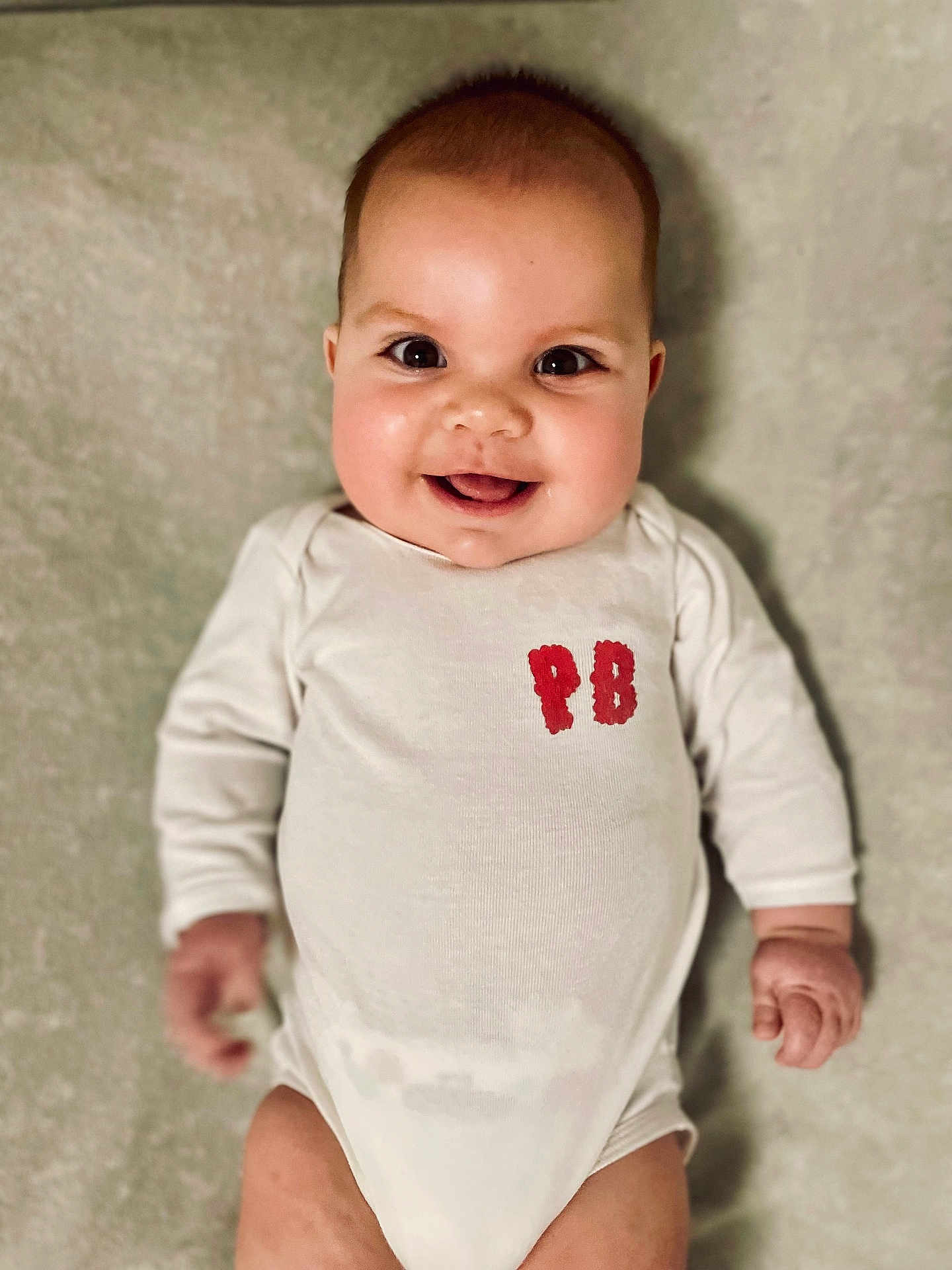 Alice participe au concours pour gagner de l'argent avec cette photo : baby, infant, smiling, onesie, face, cute, chubby_cheeks, lying_down, happy, child, young_child, indoor, human, portrait, skin, hands, eyes, head, clothing, white