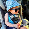 toddler, child, car_seat, sunglasses, bucket_hat, blue_clothing, seatbelt, sunlight, smile, curly_hair, car_interior, safety, summer, casual, happy, cute, portrait, sunshine, travel, fashion
