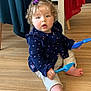 toddler, child, curly_hair, hair_clip, blue_shovel, plastic_toy, sitting, wooden_floor, indoor, clothing, pants, long_sleeve, purple, red_cloth, chair, foot, hand, face, expression, home